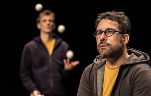 Photo du spectacle L'envers de nos décors de Clément Dazin et Thomas Scotto. Deux hommes sont sur des tables en pin avec des boules de jonglages.